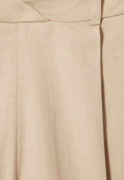Primer plano de pantalones de tela beige que muestran detalles de pinzas y cintura con trabilla para cinturón.