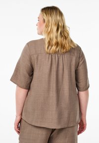 Short-sleeve brown blouse made of textured fabric, featuring a yoke detail and a relaxed fit. Back yoke gathers add fullness.