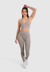 Beige geribbelde sport-bh en hoge taille legging combinatie met een aansluitend ontwerp, gecombineerd met witte sportschoenen. Studioachtergrond.