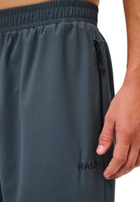 Szare spodenki sportowe z teksturowanym wzorem siatki, elastycznym pasem i zasuwana kieszenią boczną. Posiadają logo "HALO" w kolorze czarnym.