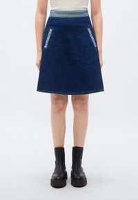 Τζιν φούστα σε γραμμή Α σε σκούρο μπλε χρώμα με ανοιχτό μπλε τζιν μέση και δύο μπροστινές τσέπες. Συνδυάστε με μαύρα μποτάκια αστραγάλου.