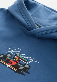 Hoodie bleu avec un graphique de voiture de course et broderie. Texture lisse, capuche avec cordon de serrage, et texte « Racing » en blanc.