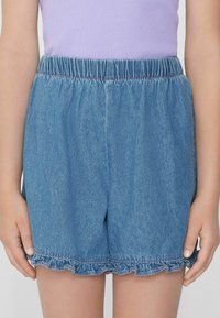 Džínové šortky s elastickým pasem, volánkovým lemem a světle modrou barvou. Obsahují decentní růžové prošívání podél lemu.
