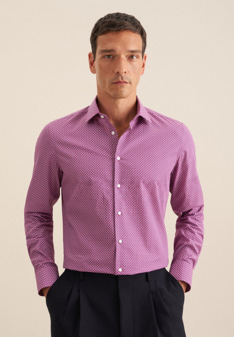 Chemise à manches longues pour homme en tissu rose à motif, avec un col déployé et des boutons blancs, associée à un pantalon sombre.