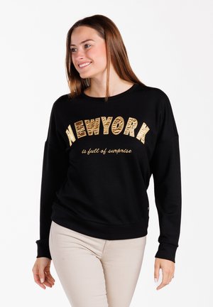 Sudadera negra de tejido suave que presenta texto bordado en dorado "NEWYORK" y "está llena de sorpresas" en una fuente estilizada, corte holgado.