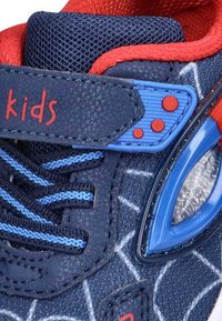 Zapatos sintéticos azules para niños con acentos rojos, textura de malla, cordones azules y correa, y un patrón de telaraña. Cuenta con un elemento que se ilumina.