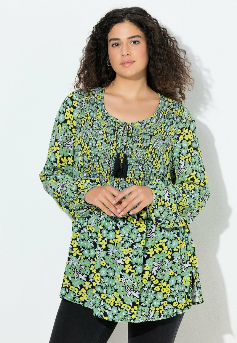 Tunika floreale in verde, giallo e nero, con maniche lunghe, dettagli arricciati e scollatura cinchata con dettagli a nastro.
