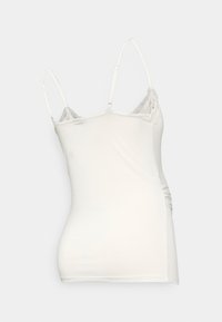 Camisole bianca con spalline sottili, texture morbida e dettagli in pizzo sul collo, caratterizzata da un design aderente e leggeri arricciature sul lato.