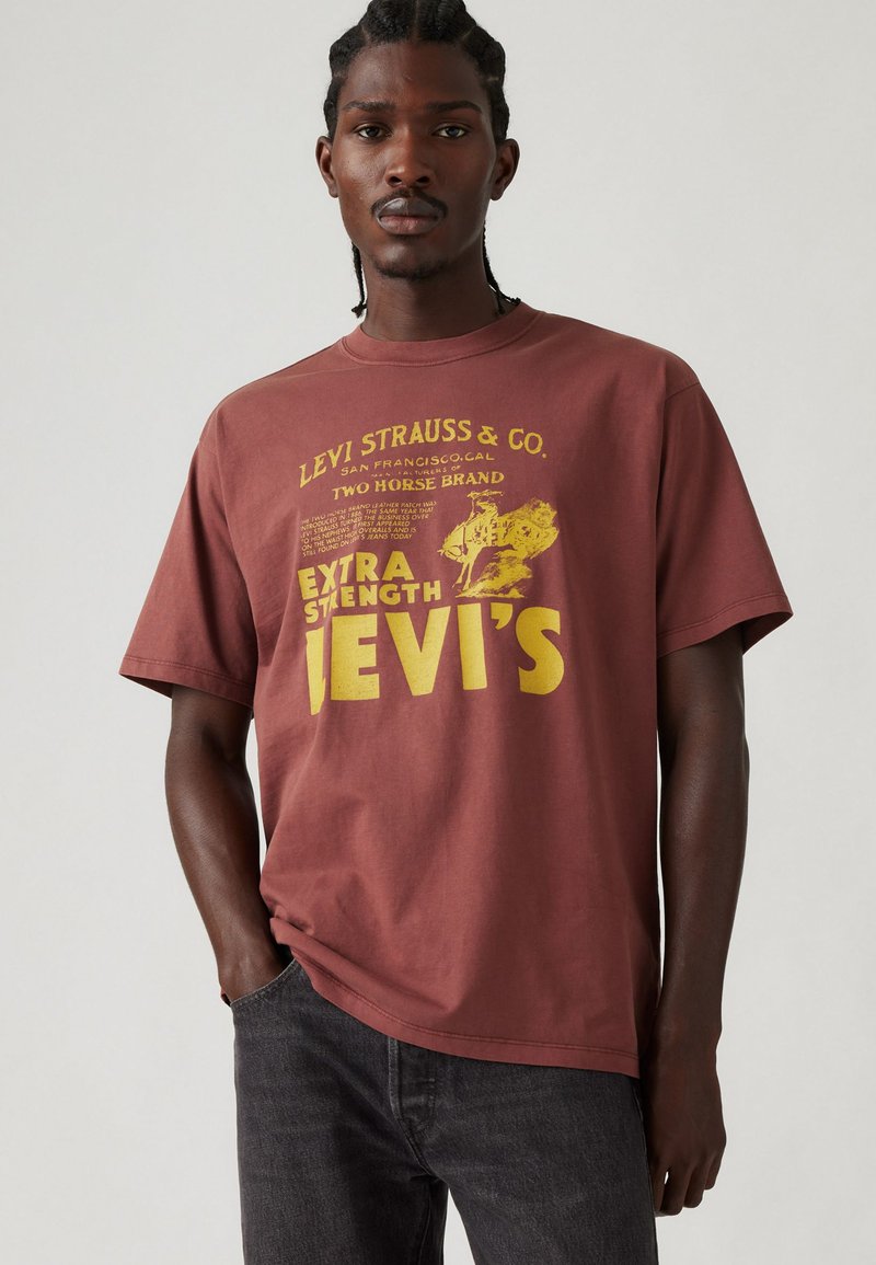 Camiseta de algodón color burdeos con mangas cortas; presenta texto gráfico en amarillo y elementos de diseño que representan la marca Levi's.