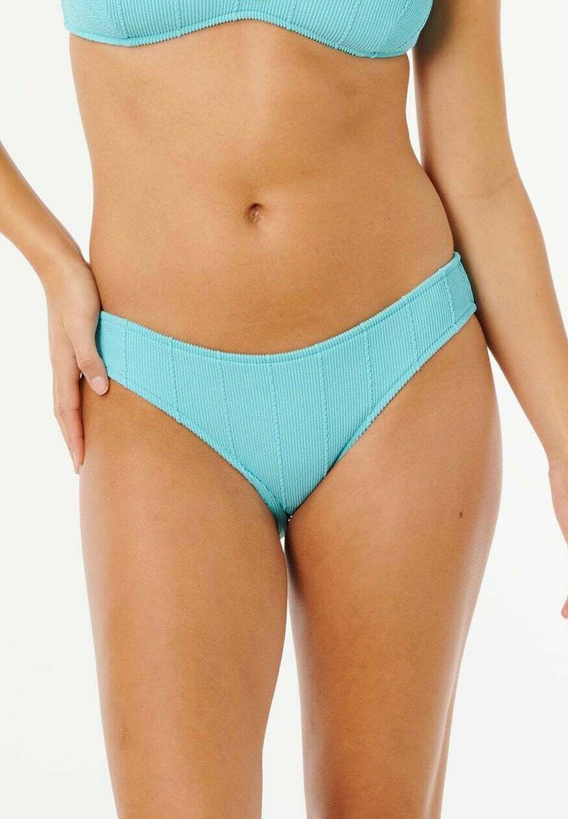 Kvinde iført turkis ribbet bikiniunderdel og -top, vist fra mellemgulvet til de øverste lår med den ene hånd hvilende på hoften.