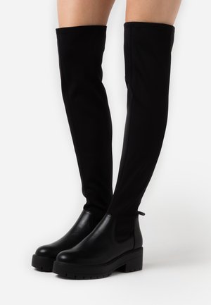 Zwarte boven-de-knie laarzen met een gladde leren afwerking en elastische stof, voorzien van een chunky zool en trekhaakjes voor gemakkelijk aan- en uittrekken.