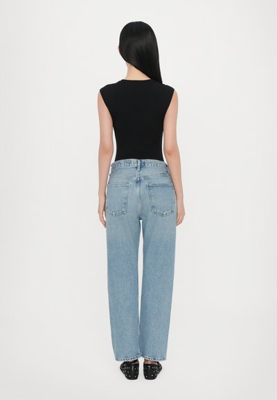 Μαύρο αμάνικο τοπ σε συνδυασμό με ανοιχτό μπλε ψηλόμεσα τζιν με φαρδιά ποδάρια. Τα τζιν έχουν πίσω τσέπες και ξεφτισμένα τελειώματα. Μαύρα παπούτσια χωρίς κορδόνια με καρφιά.