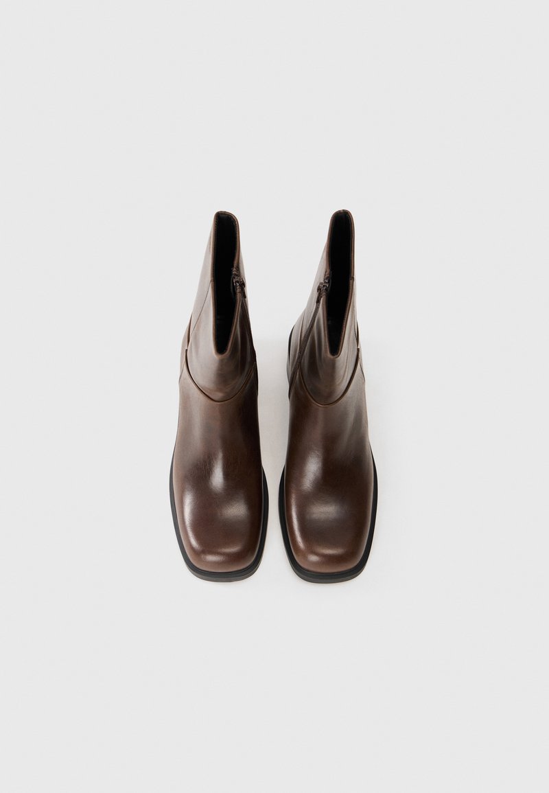 Brązowe skórzane botki za kostkę o gładkiej fakturze, kwadratowym nosku i bocznymi zamkami, na jednolitym białym tle.