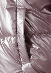 Gros plan sur une poche de veste matelassée mauve brillante avec des coutures visibles et une texture de tissu rembourré lisse.