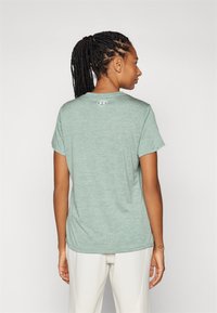 Camiseta atlética de manga corta en verde claro, con cuello redondo y una sutil textura jaspeada. Presenta un pequeño logo en la parte posterior del cuello.
