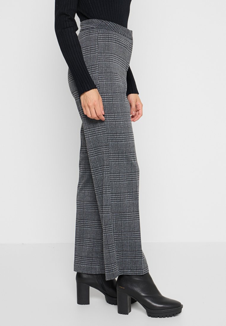 Hoch taillierte karierte Hosen in Grautönen, gefertigt aus einem strukturierten Stoff. Kombiniert mit schwarzen, schimmernden Ankle Boots mit dicker Sohle.