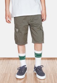 Olijfgroene cargoshorts met zijzakken, gecombineerd met witte sokken met groene strepen en grijze sneakers met witte zolen.