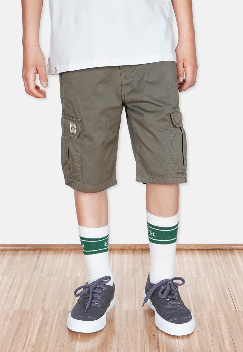 Olijfgroene cargoshorts met zijzakken, gecombineerd met witte sokken met groene strepen en grijze sneakers met witte zolen.
