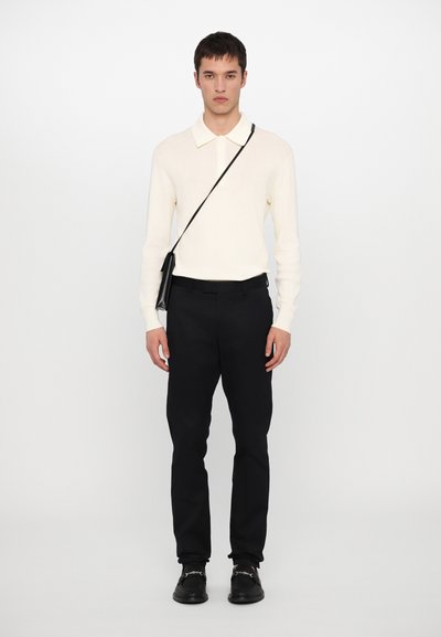 Krämfärgad stickad pullover med krage, tillsammans med svarta byxor. Svart axelremsväska med platt design, svarta loafers. Enkelt monokromt utseende.