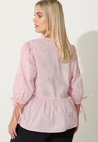 Blusa rosa con maniche a sbuffo, vita elastica e ricamo a forma di fiocchi argentati. Presenta lacci ai polsini e una texture di tessuto leggero.