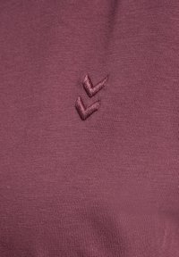 Bordo tkanina o gładkiej fakturze z małym, haftowanym podwójnym szewronem w tym samym kolorze. Zbliżenie na tekstylia.