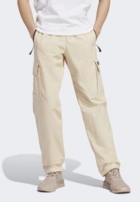 Pantalones cargo beige con cintura elástica, dos bolsillos laterales y bolsillos cargo adicionales en las piernas. La tela tiene una textura suave.