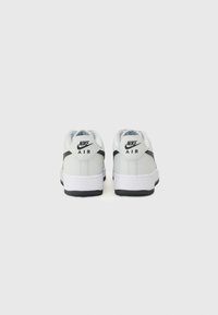 White leather Nike Air sneakers with a black accent along the heel, featuring a rounded toe and a textured sole. Back view shown.