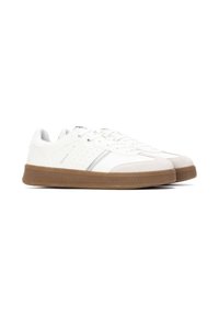 Zapatillas bajas blancas con punteras de ante gris claro, lados perforados y suelas de goma marrón, mostradas una al lado de la otra sobre un fondo blanco.