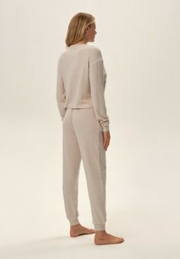 Beżowy zestaw dresowy z prążkowanego materiału, składający się z krótkiej bluzki i zwężających się spodni z długimi rękawami i elastycznymi mankietami. Miękka tekstura, minimalistyczny design.