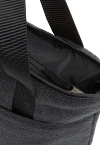 Bolsa de vellón negra con un exterior texturizado, que cuenta con un bolsillo con cremallera en el interior y amplias correas de nylon para transportar.