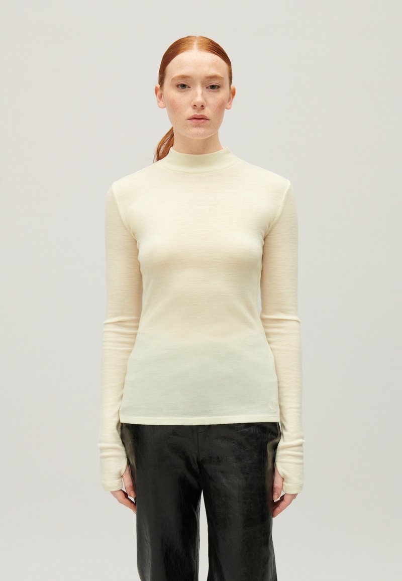 Crème-kleurige lang mouwtop met hoge hals en een aansluitend ontwerp. Gemaakt van zachte, gladde stof, met extra lange boorden.