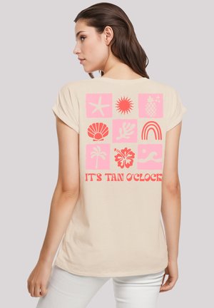 Beige cotton t-shirt featuring a back graphic with pink beach-themed icons and "IT'S TAN O'CLOCK" in a bold red font. Short sleeves, relaxed fit.