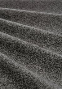Tissu gris texturé avec des motifs subtils, plié pour révéler profondeur et douceur. Le tissage compact ajoute une qualité tactile.