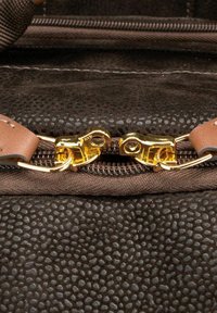Tessuto marrone con una finitura lucida, caratterizzato da una cerniera in stile vintage di colore oro e un accentuazione in pelle sulla linguetta di apertura.