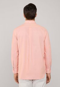 Camisa de manga larga rosa claro con cuello botón, pliegue en la espalda y detalle de puño en contraste. Fabricada con un tejido suave.