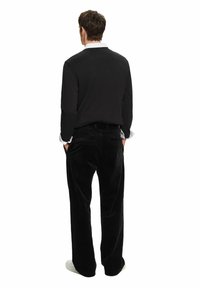 Mustat corduroy-housut, joissa on leveät lahkeet, yhdistettynä mustaan pitkähihaiseen paitaan, jossa on valkoinen kaulus. Yksinkertainen muotoilu, minimaaliset korostukset ja rento ilme.