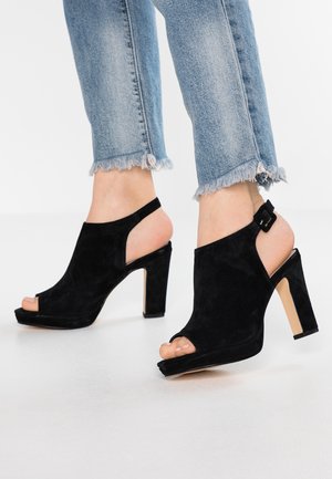 Černé nubukové sandály na podpatku s otevřenou špičkou a designem se zadním páskem, které mají pevný blokový podpatek a detaily s přezkou na pásku kolem kotníku.