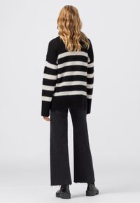Pull à rayures noires et blanches en matière duveteuse avec une coupe décontractée. Associé à un pantalon noir à jambes larges et des bottes noires épaisses.