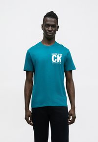Tyrkysové bavlnené tričko s krátkymi rukávmi a okrúhlym výstrihom. Na prednej strane je biely nápis "CK" a text "CALVIN KLEIN Established 1968."
