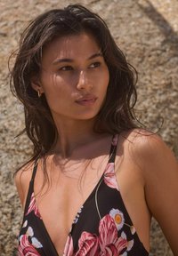 Costume da bagno floreale nero con fiori tropicali rosa e bianchi, design a profondo scollo a V e spalline sottili. Pelle visibile su spalle e collo.