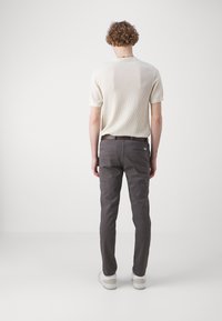 Hellbeige, gerippter Kurzarm-Top kombiniert mit dunkelgrauen, schmal geschnittenen Hosen. Das Outfit wird durch weiße Sneaker und einen braunen Gürtel ergänzt.