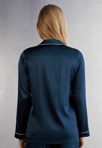 Nattlinne i marinblå satin med långa ärmar och krage, prydnad med vit piping längs kragen och ärmslut. Slät struktur, avslappnad passform.