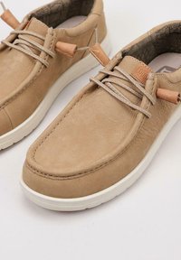 Scarpe in pelle color cuoio con una texture liscia, dotate di punta arrotondata, lacci beige, dettagli in pelle e suola in gomma bianca.