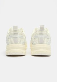 Sneaker bianche in mesh con tessuto texturizzato, linguette posteriori per il richiamo e suole in gomma spessa color crema. Design minimalista con accenti sottili.