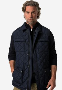 Marinblå quiltad väst med knappkrage, två bröstfickor, dragkedjestängning och sidofickor; kombinerad med en marinblå tröja under.