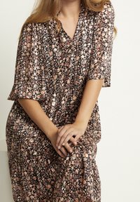 Schwarzes Blumenkleid mit kurzen Ärmeln, das mit pinken und weißen Blumen verziert ist. Fließender Stoff mit weicher Textur, an der Taille gerafft.