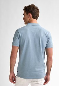 Světle modrá polokošile vyrobená z texturované tkaniny, s krátkým rukávem a klasickým límcem. Malé boční rozparky na lemu pro pohodlnější pohyb.