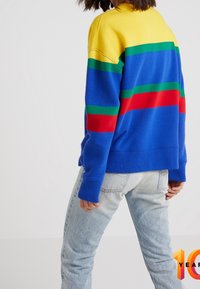 Flerfärgad sweatshirt med rund halsringning som har en gul överdel, blå kropp och horisontella ränder i grönt, rött och blått. Tillverkad av mjukt tyg.