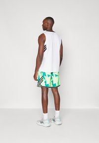 Ärmelloses weißes Tanktop mit schwarzen Streifen; grüne gemusterte Shorts; graue Sneakers mit hellblauen Akzenten; Sportbekleidung.