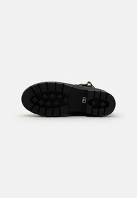 Black rubber outsole with deep treads for traction, featuring a textured surface and engraved logo. Flat and durable design for stability.
